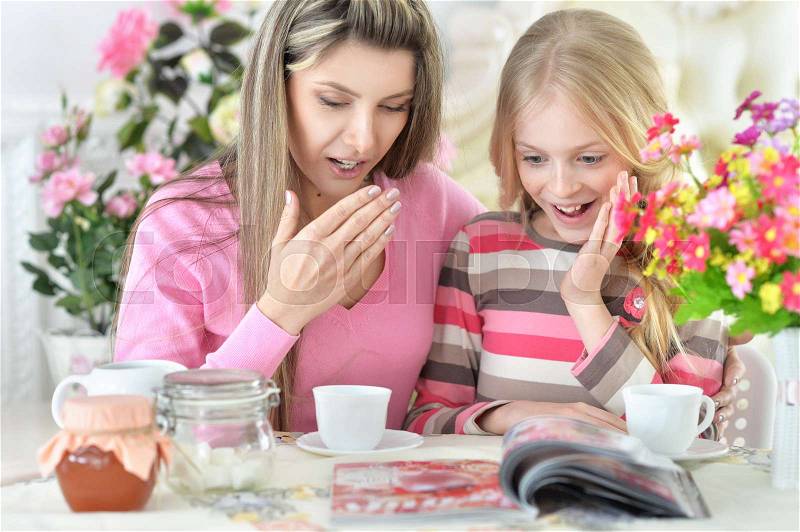 Mom and daughter watch the magazine at the table, stock photo