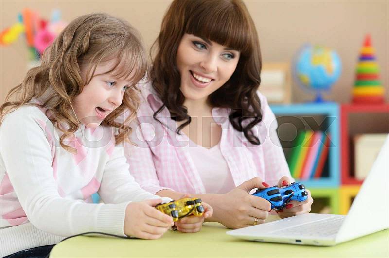 Mother and daughter playing at table with laptop, stock photo