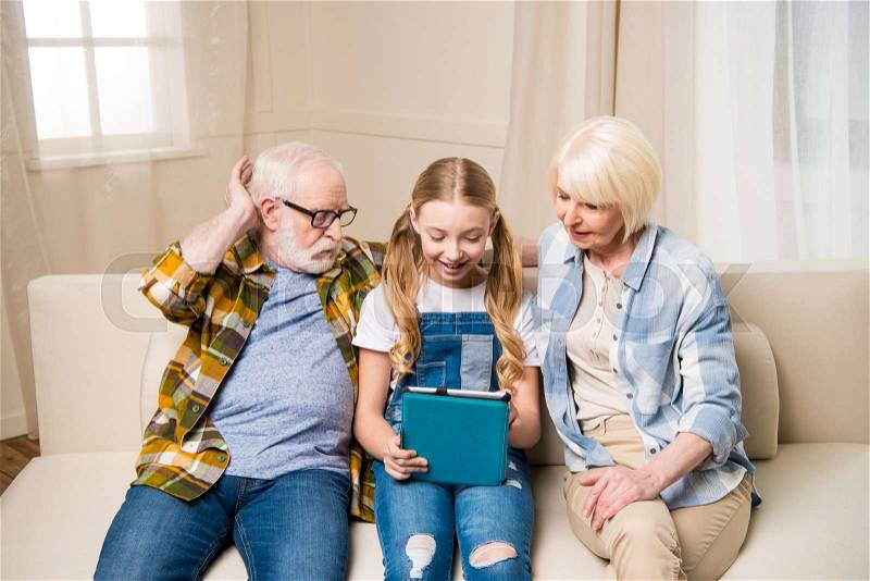 Happy grandparents and granddaughter using digital tablet together at home, stock photo