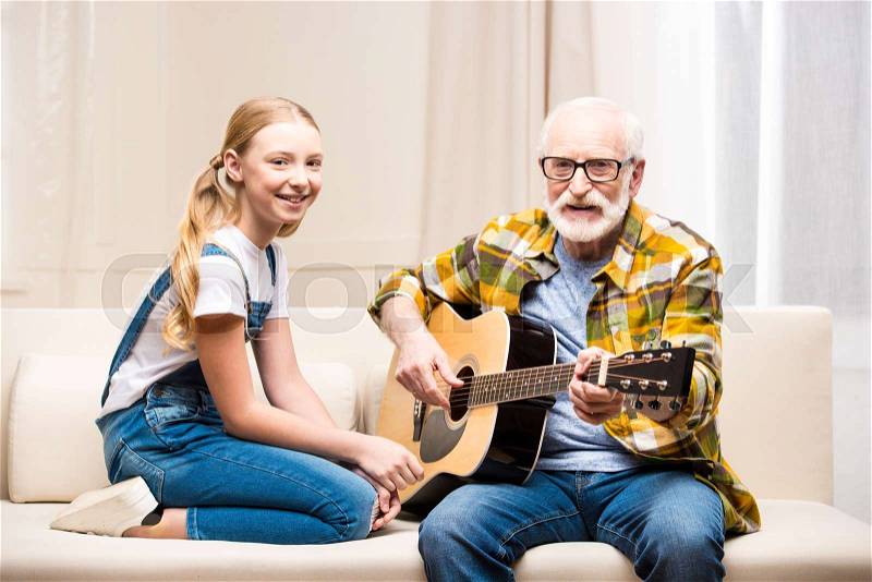 Senior man in eyeglasses teaching cute little granddaughter playing acoustic guitar , stock photo
