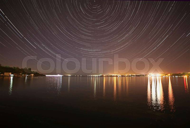 Tracks of stars in night sky above river, stock photo