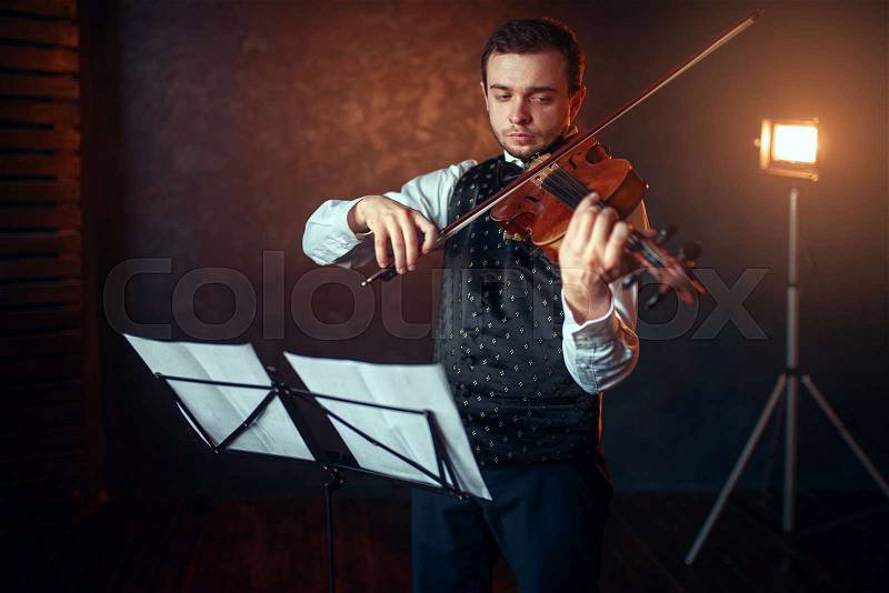 Portrait of male violinist with violin against music stand. Fiddler man with musical instrument playing in studio, solo concert training, stock photo