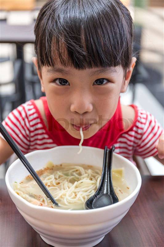 Asian little Chinese girl eating noodles soup in outdoor cafe, stock photo