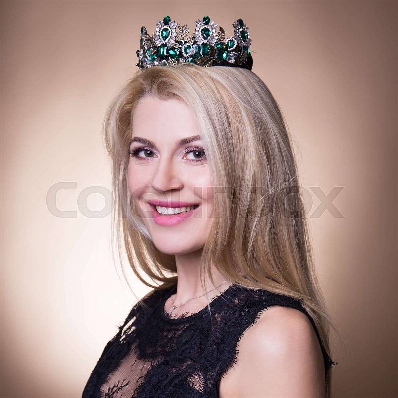 Close up portrait of young beautiful blond woman with crown over beige background, stock photo