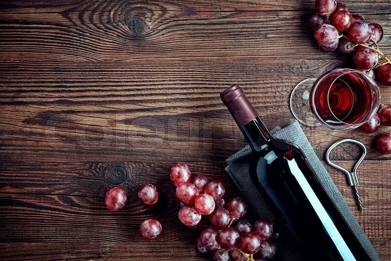 Bottle and glass of red wine and grapes on wooden background from top view, stock photo