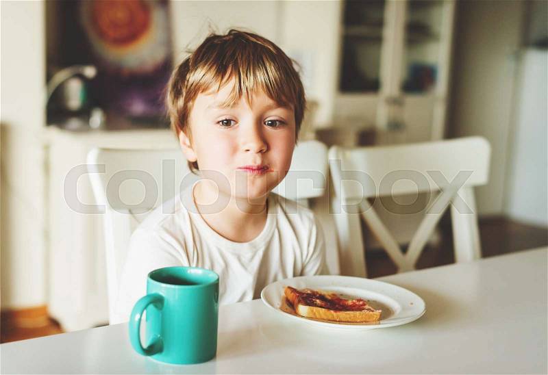 Cute little boy eating his toast with jam and hot chocolate for breakfast, stock photo