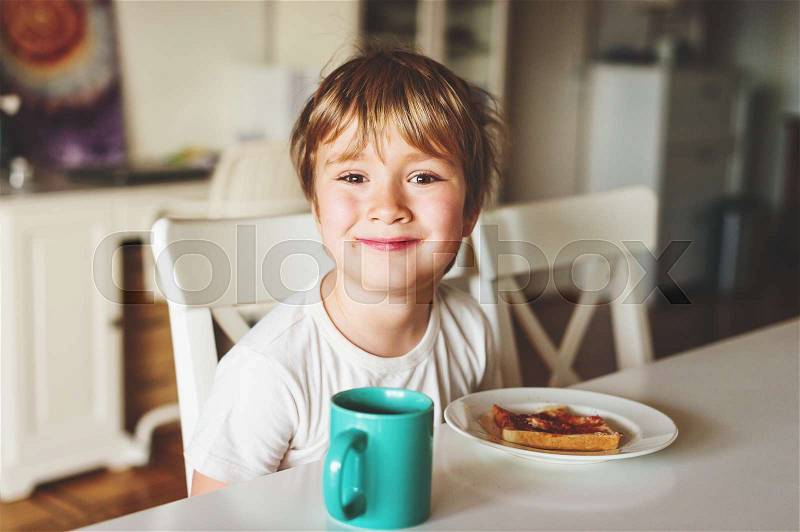 Cute little boy eating his toast with jam and hot chocolate for breakfast, stock photo