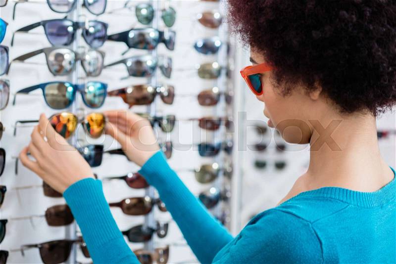 Black woman wearing and buying sunglasses in optician shop, stock photo