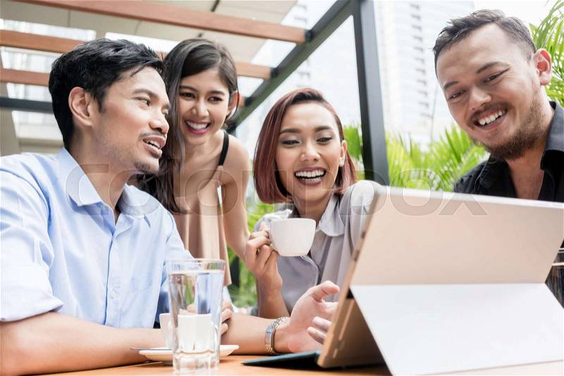 Group of four young Asian people having fun while sitting together outdoors at a coffee shop with wireless internet connection, stock photo