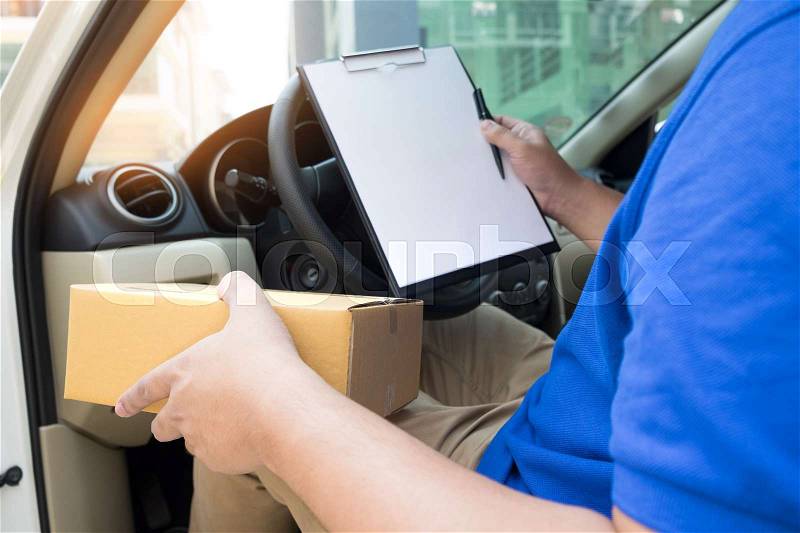 Delivery man with cardboard box checking document list In van and parcels on seat outside the warehouse, stock photo