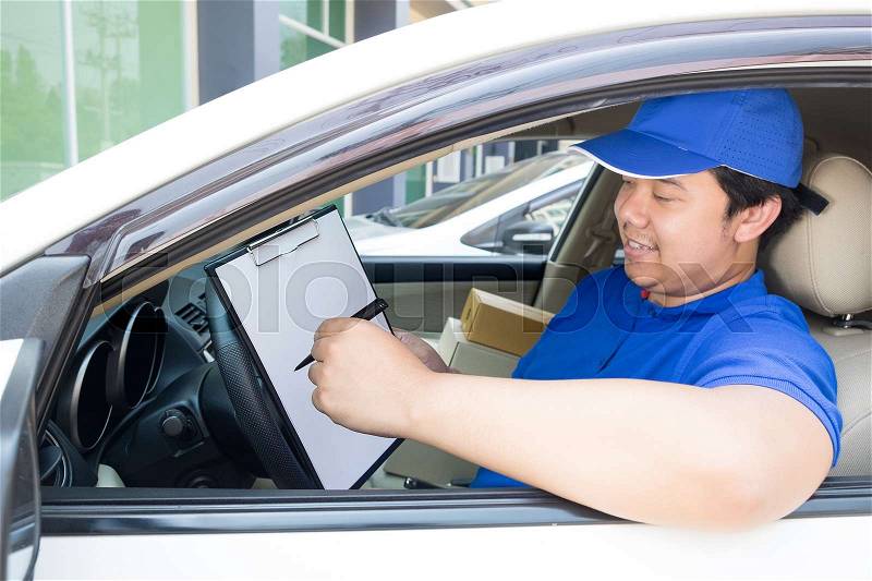 Delivery man with cardboard box checking document list In van and parcels on seat outside the warehouse, stock photo