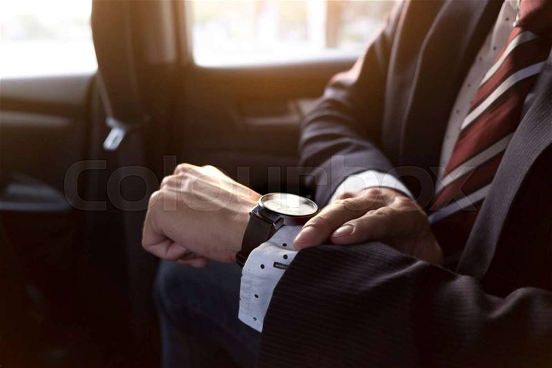 Handsome businessman looking on wrist watch in car, stock photo