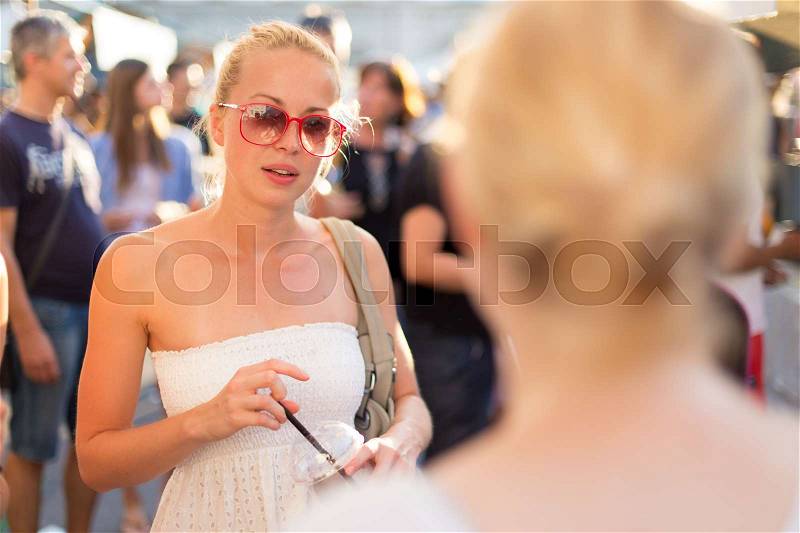 It is nice to see you. It has been a while. Two happy young female friends enjoying a conversation on urban food market at random after work encounter. Pleasant free time socializing, stock photo