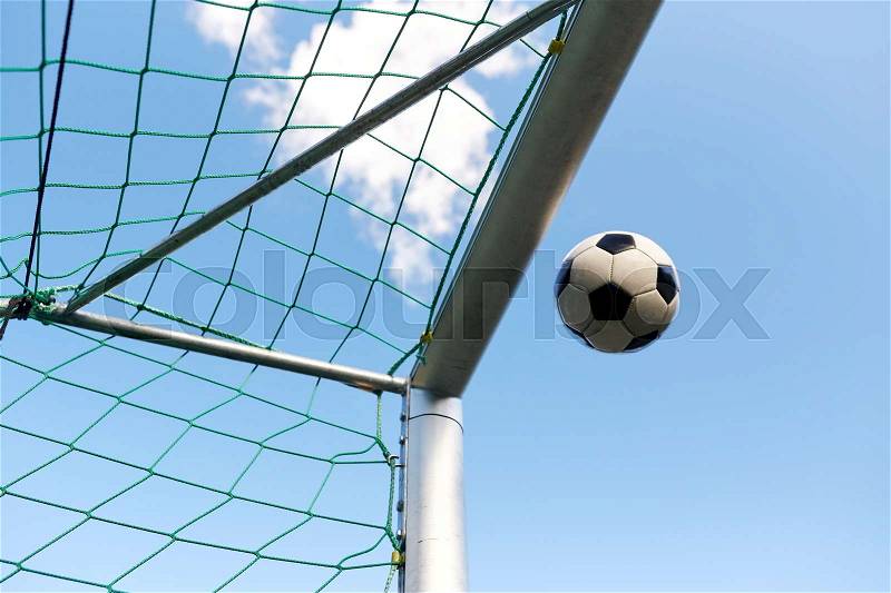 Sport, soccer and game - ball flying into football goal net over blue sky, stock photo