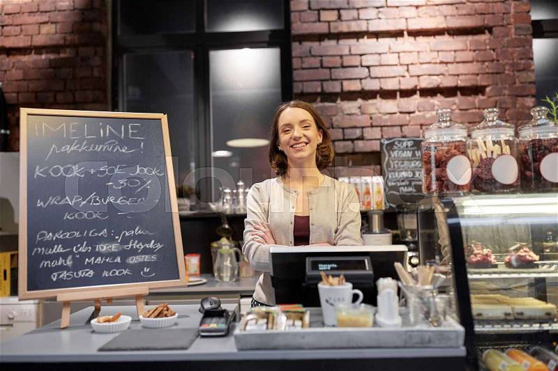 Small business, people and service concept - happy woman or barmaid at counter with cashbox in cafe or coffee shop, stock photo