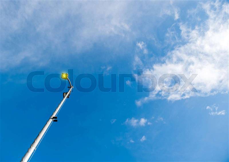 Lighting pole LED street lamp seen from below against blue spring sky with beautiful cloud - yellow pure light coming from the bulb, stock photo