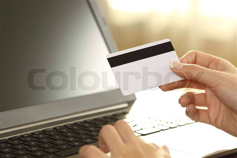 Girl hands holding credit card and buying on line sitting on a couch in the living room at home with a warm light in the background, stock photo