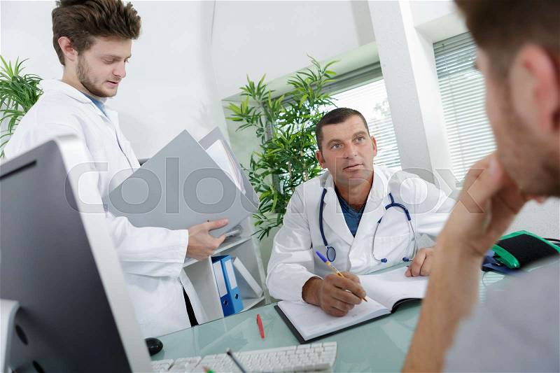Doctor in consultation with patient, student doctor holding notes, stock photo