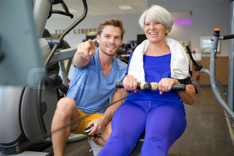 Personal trainer with senior woman using rowing machine, stock photo