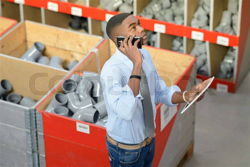 Man in pipe fittings department, holding tablet and speaking on telephone, stock photo