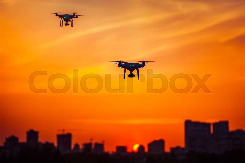 Two modern Remote Control Air Drones Fly with action cameras in dramatic orange sunset sky. Cityscape silhouette in the background. Modern technologies. Kiev, Ukraine. Travel, hobby, inspiration, stock photo