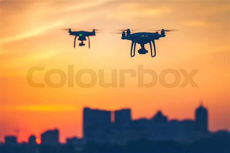 Two modern Remote Control Air Drones Fly with action cameras in dramatic sunset sky. Cityscape silhouette in the background. Modern technologies. Close up. Kiev, Ukraine. Travel, hobby, inspiration, stock photo