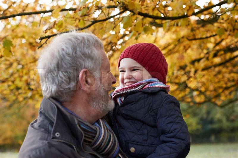 Grandfather Cuddling Granddaughter On Autumn Walk, stock photo