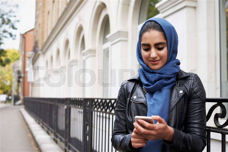 British Muslim Woman Using Mobile Phone In Urban Setting, stock photo