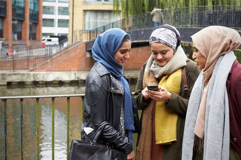 Muslim Female Friends Using Mobile Phone In Urban Setting, stock photo