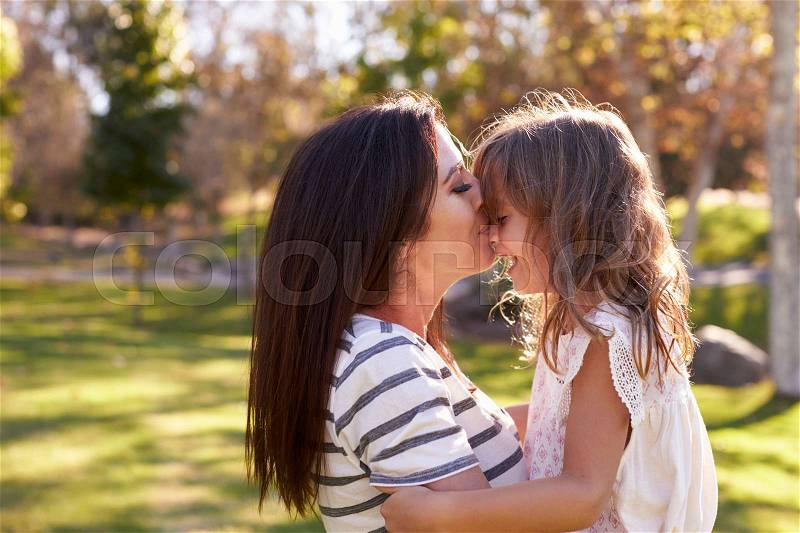 Loving Mother Kissing Daughter In Park, stock photo