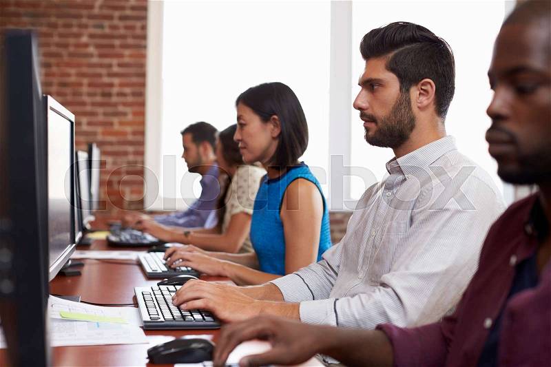 Staff Sitting At Desks Using Computers In Busy Office, stock photo