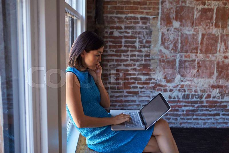 Businesswoman By Window Using Mobile Phone And Laptop, stock photo