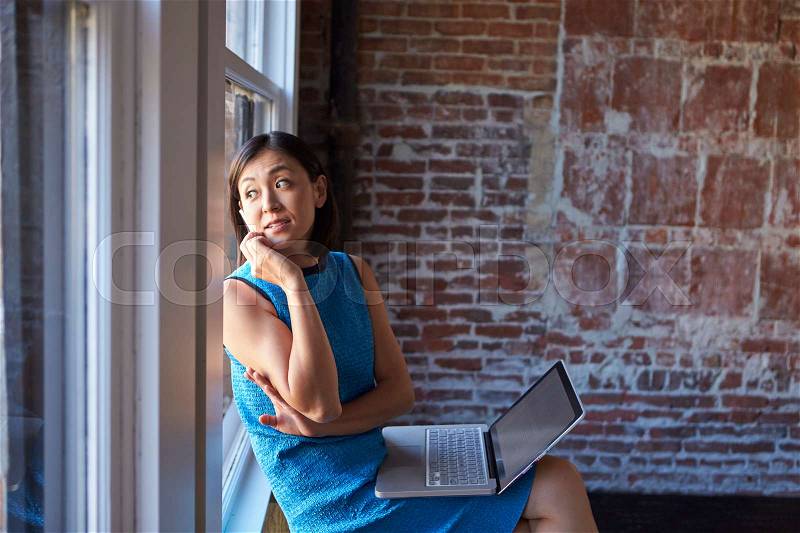 Businesswoman In Office Sitting By Window Using Laptop, stock photo