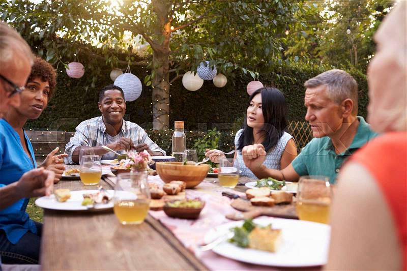 Group Of Mature Friends Enjoying Outdoor Meal In Backyard, stock photo