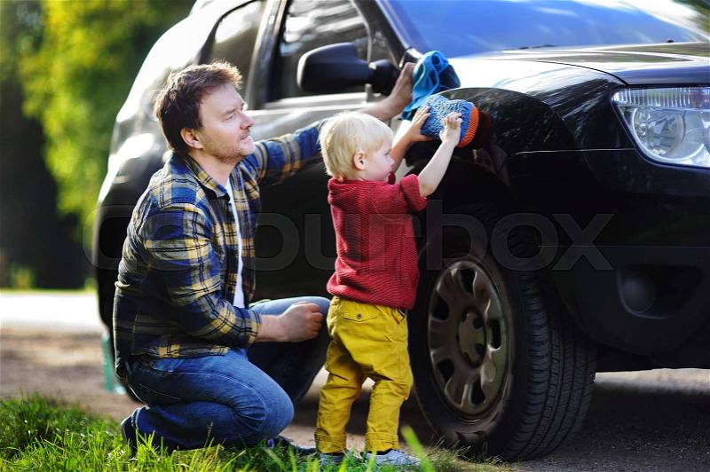 Middle age father with his toddler son washing car together outdoors. Family together activity, stock photo