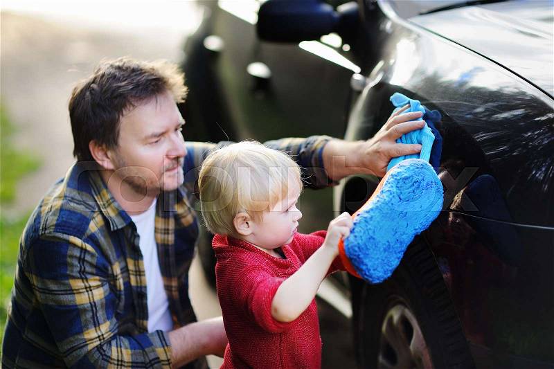 Middle age father with his toddler son washing car together outdoors. Family together activity, stock photo
