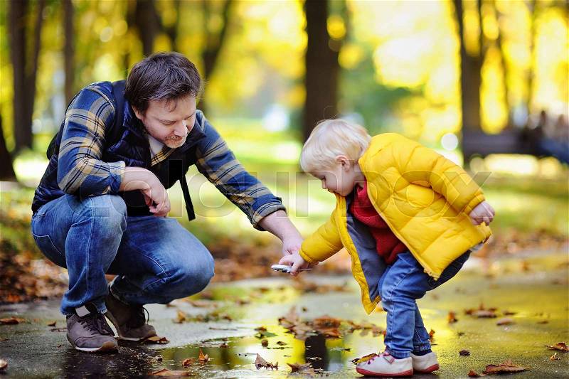 Middle age father playing with his toddler son together in a autumn park. Outdoors family leisure. Little boy playing with toy airplane, stock photo