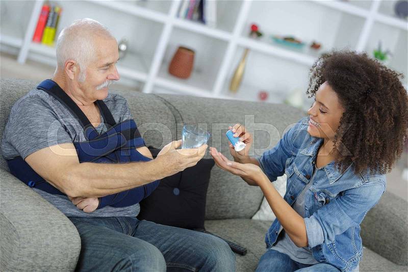 Lady preparing medication for senior man with his arm in a sling, stock photo