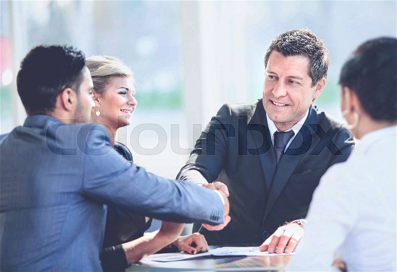 Mature businessman shaking hands to seal a deal with his partner and colleagues in a modern office, stock photo