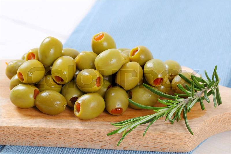 Pile of green olives stuffed with red pepper on wooden cutting board - close up, stock photo