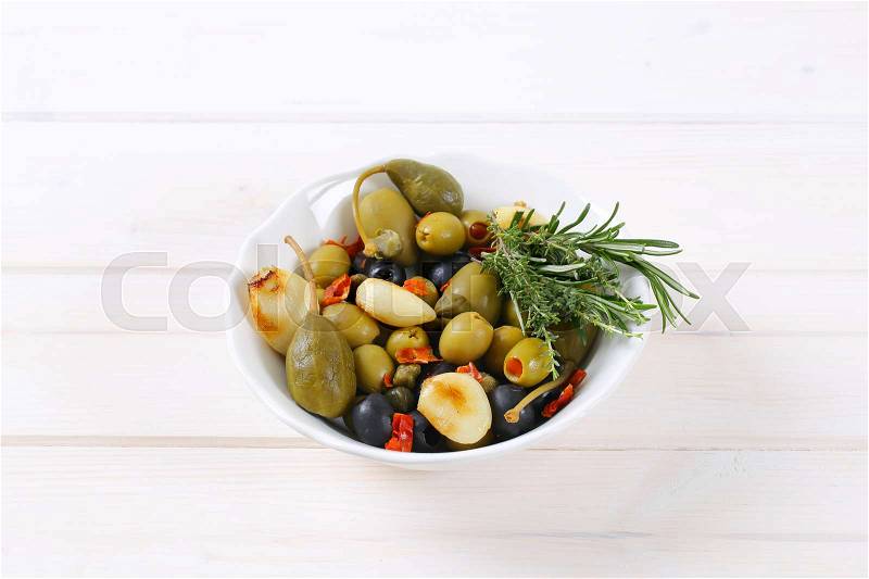 Bowl of pickled olives, capers, caper berries and garlic on white wooden background, stock photo