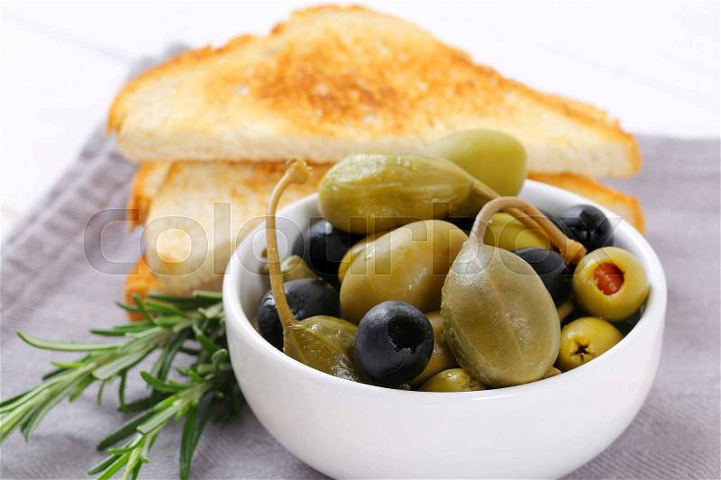 Bowl of pickled olives, capers and caper berries with toast, stock photo