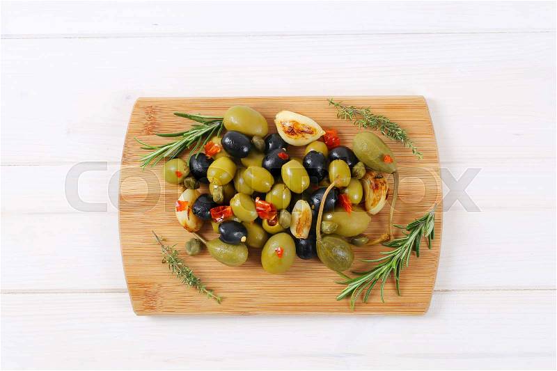 Pile of pickled olives, capers, caper berries and garlic on wooden cutting board, stock photo