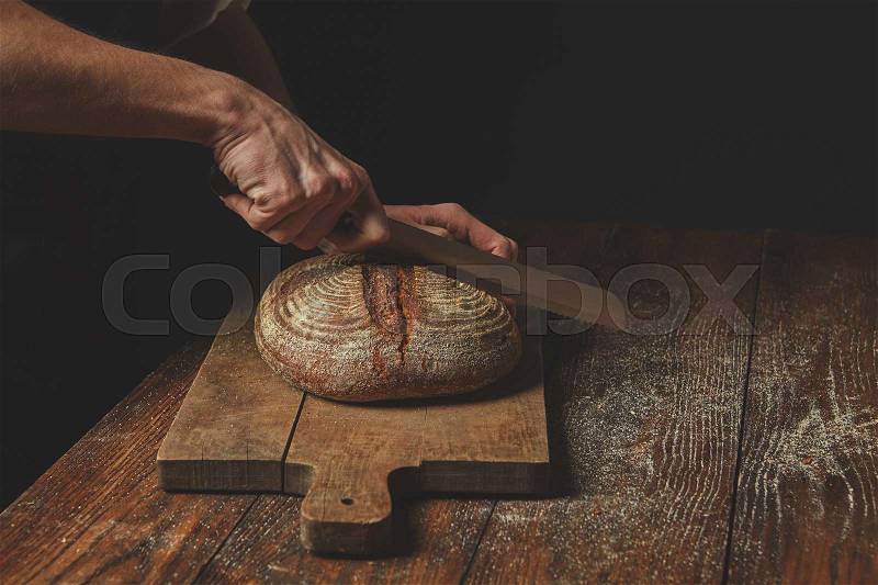 Men\'s hands cut round rye bread on a wooden brown cutting board, stock photo