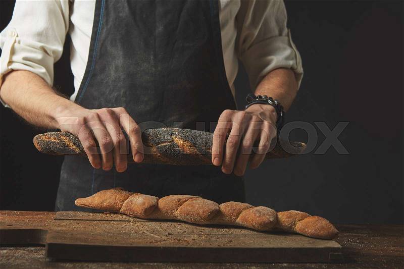 Hands breaking a warm fresh baguette. A piece of baguette on a wooden board. Best baked goods, stock photo