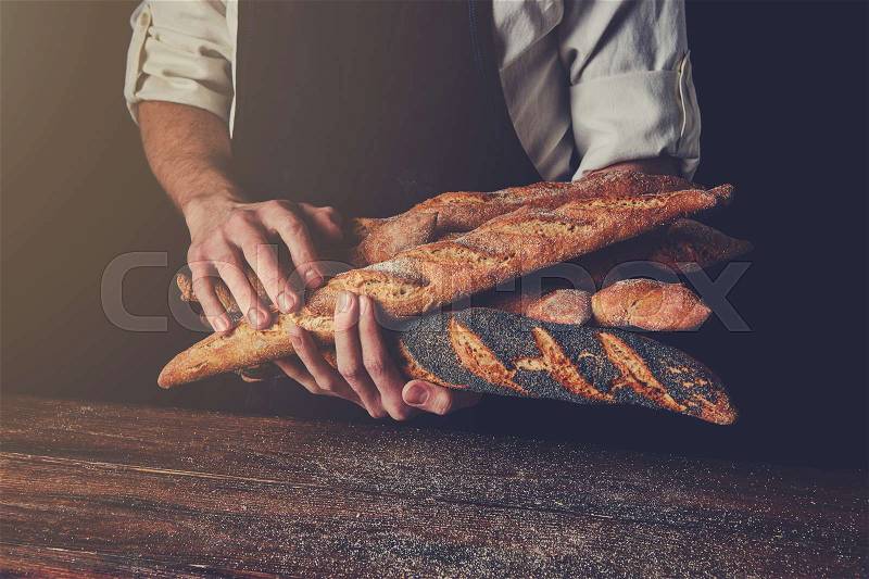 Freshly baked baguettes hold a man\'s hands against a background of a wooden table, tonned photo, stock photo