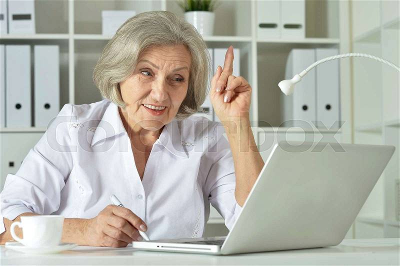 Old business woman with laptop working in the office, stock photo