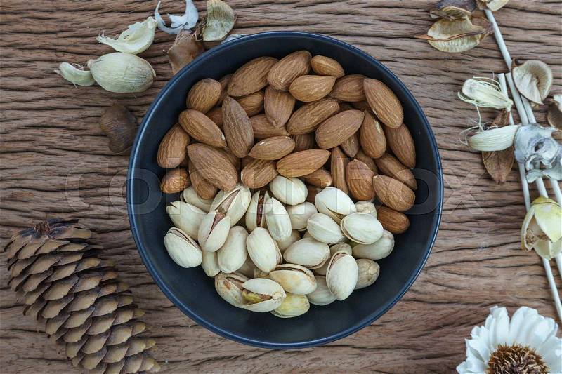 Roasted healthy delicious pistachios and almonds nuts food in black bowl on wooden table background, stock photo