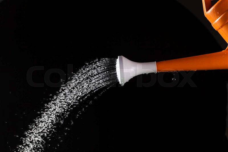 Watering can in action on black background, stock photo