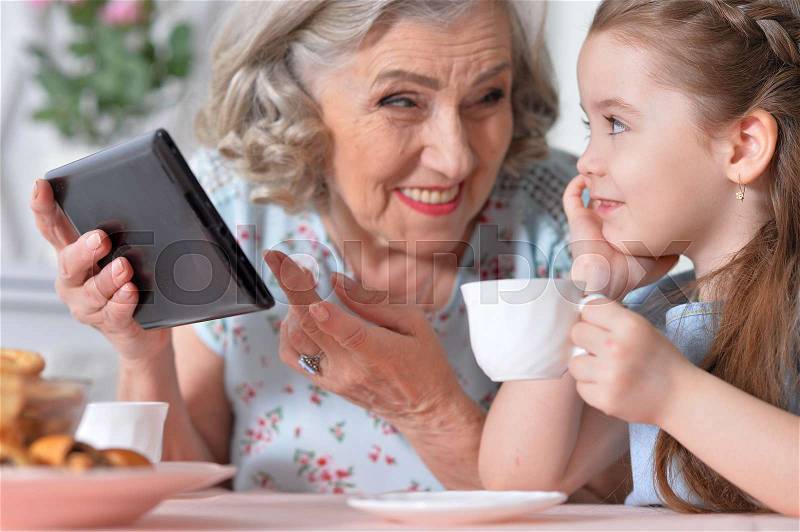 Grandmother with little granddaughter playing in a tablet computer, stock photo
